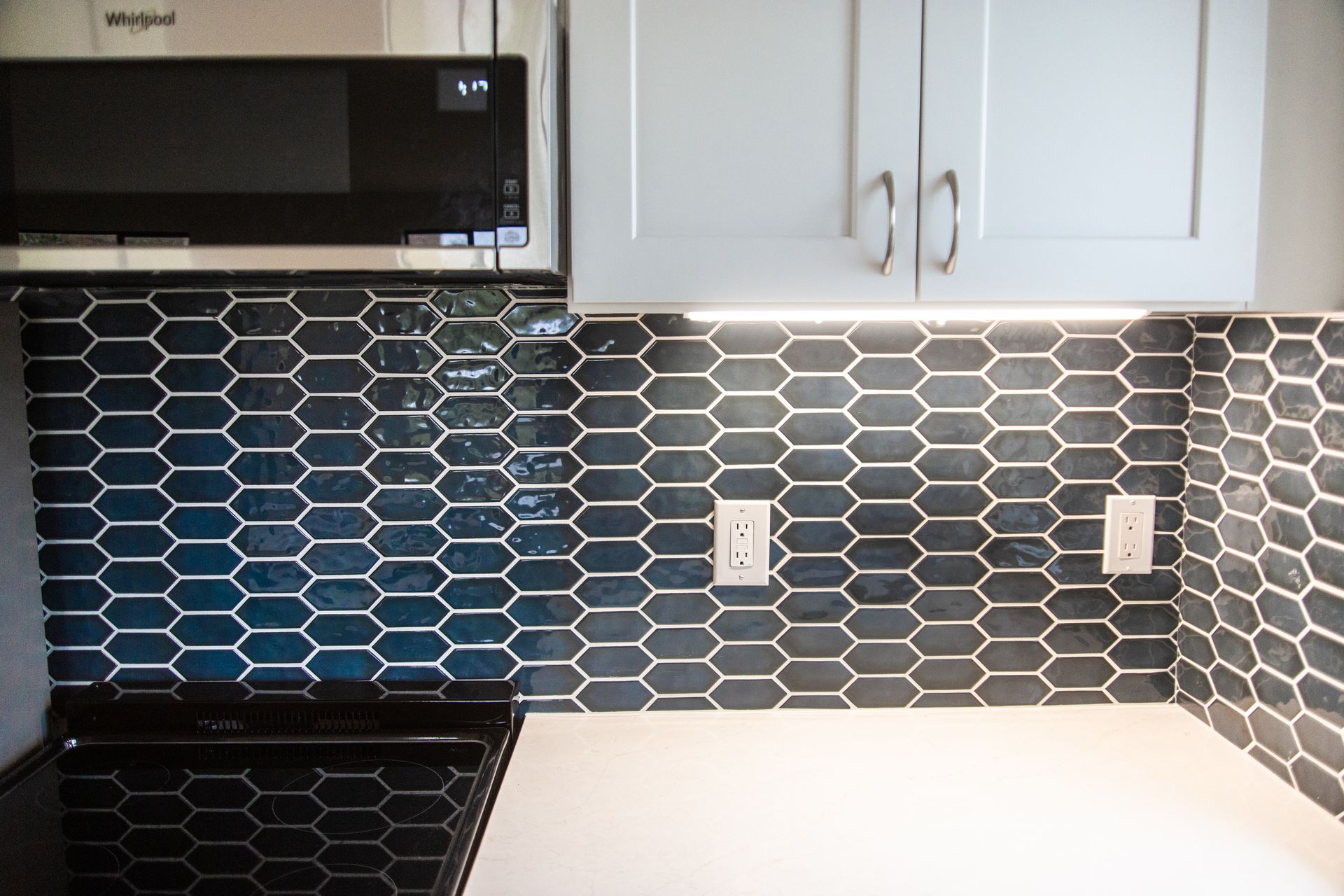A remodeled ADU kitchen with a stove, microwave, and blue tiles.