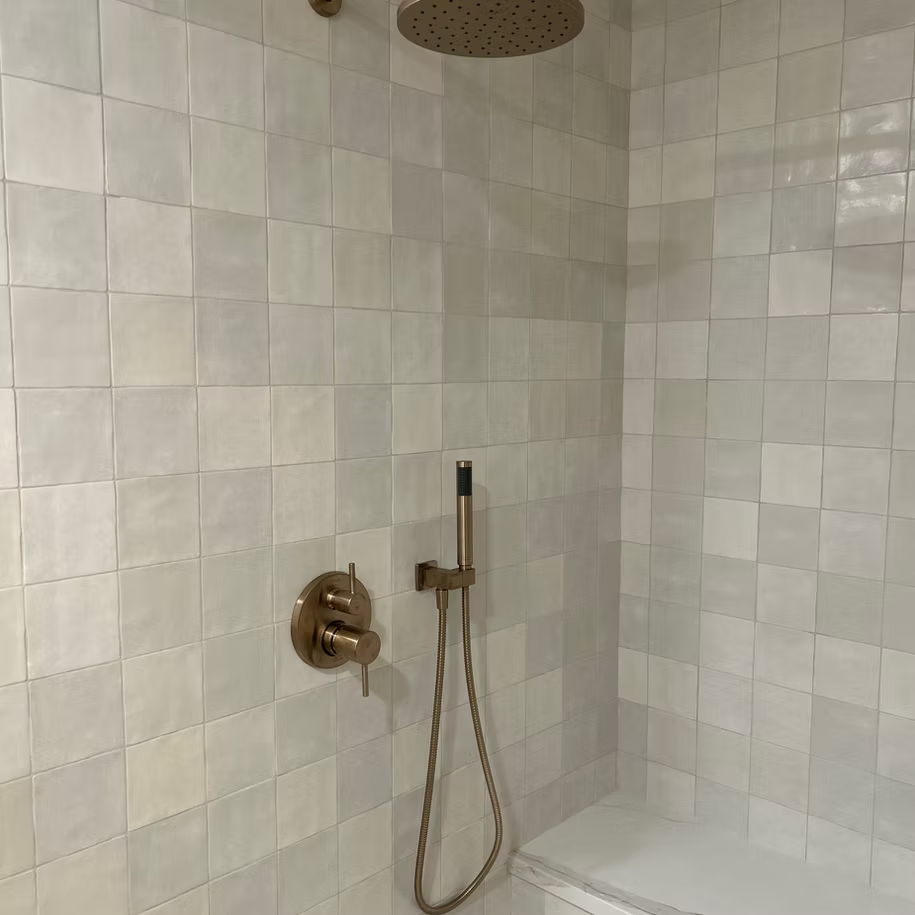 A bathroom with white tiles and a shower head.