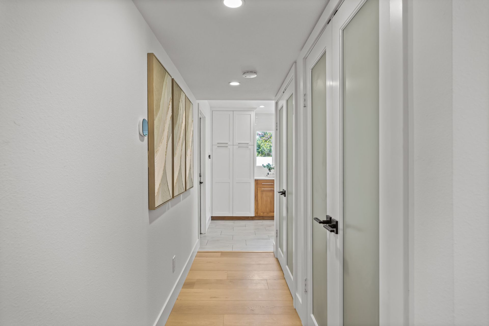 A remodeled hallway with wood floors and modern doors leading to a kitchen.