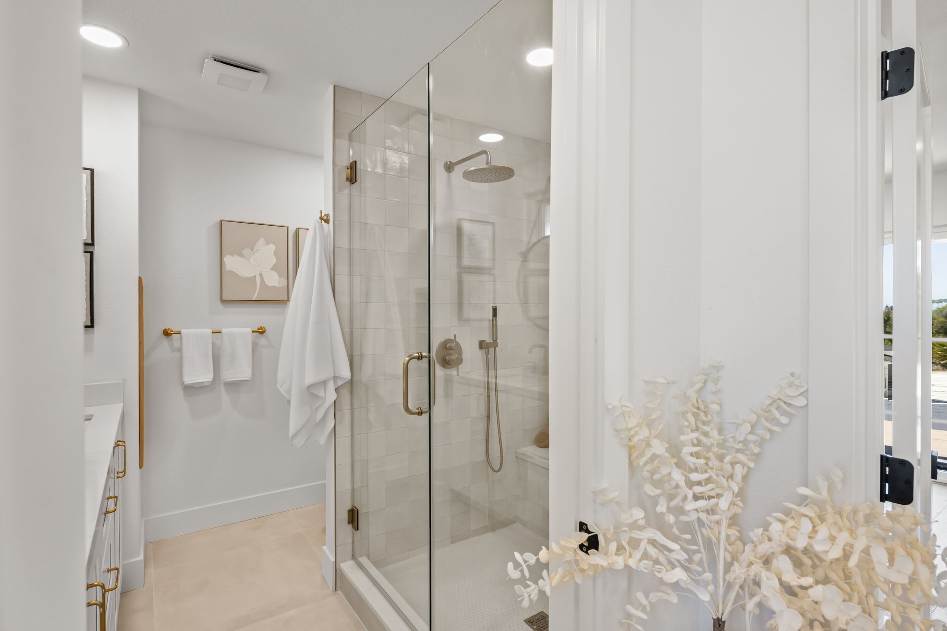 Bright bathroom with glass shower, white walls, and gold accents.