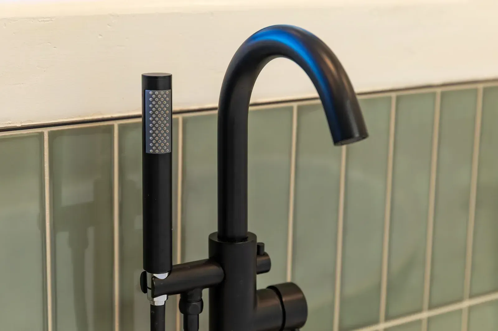 Black kitchen faucet with curved spout and pull-out spray head against tiled wall