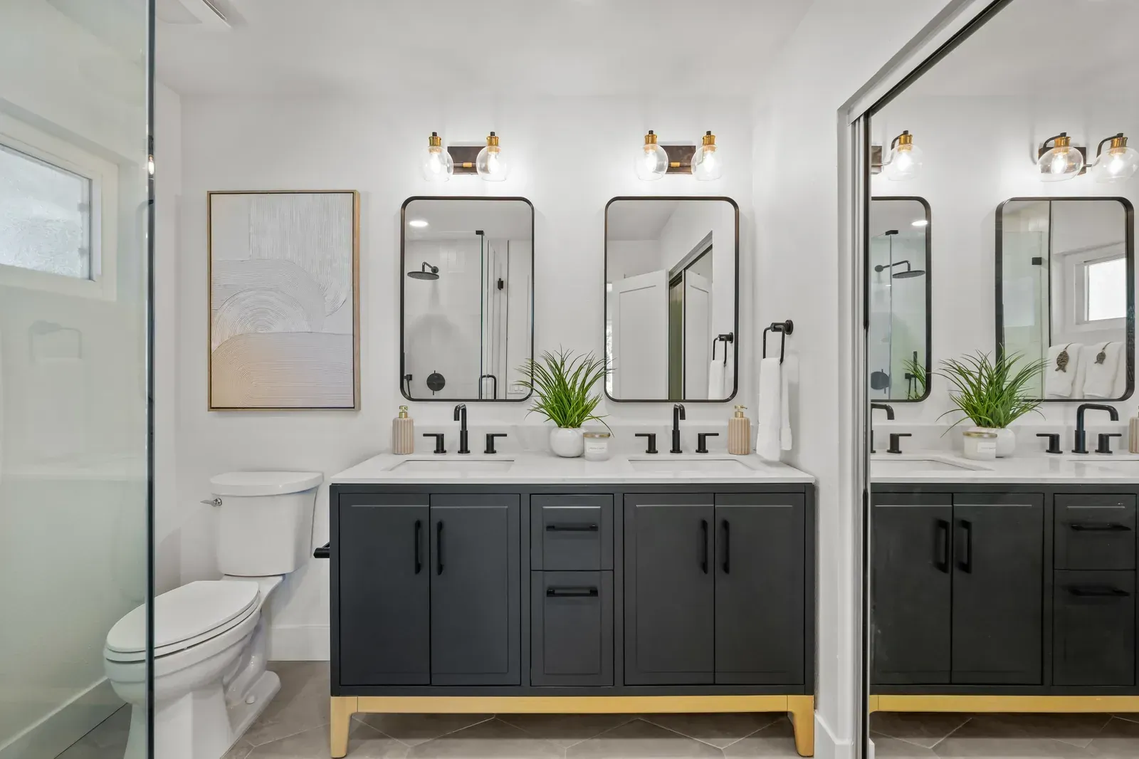 Modern bathroom with double vanity, black cabinets, mirrors, and a toilet by the shower.