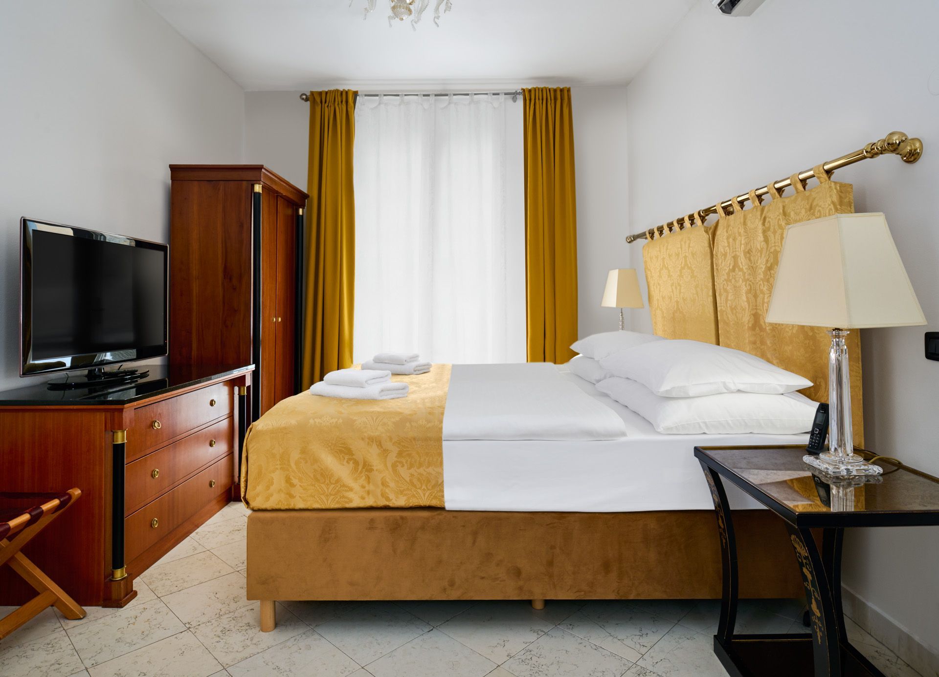 Hotel room with a bed, chair, red carpet, yellow curtains, and lamps.