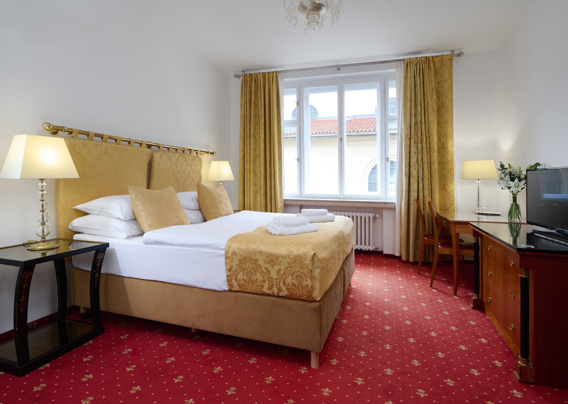 Hotel bedroom with red carpet, double bed, desk, and golden curtains.