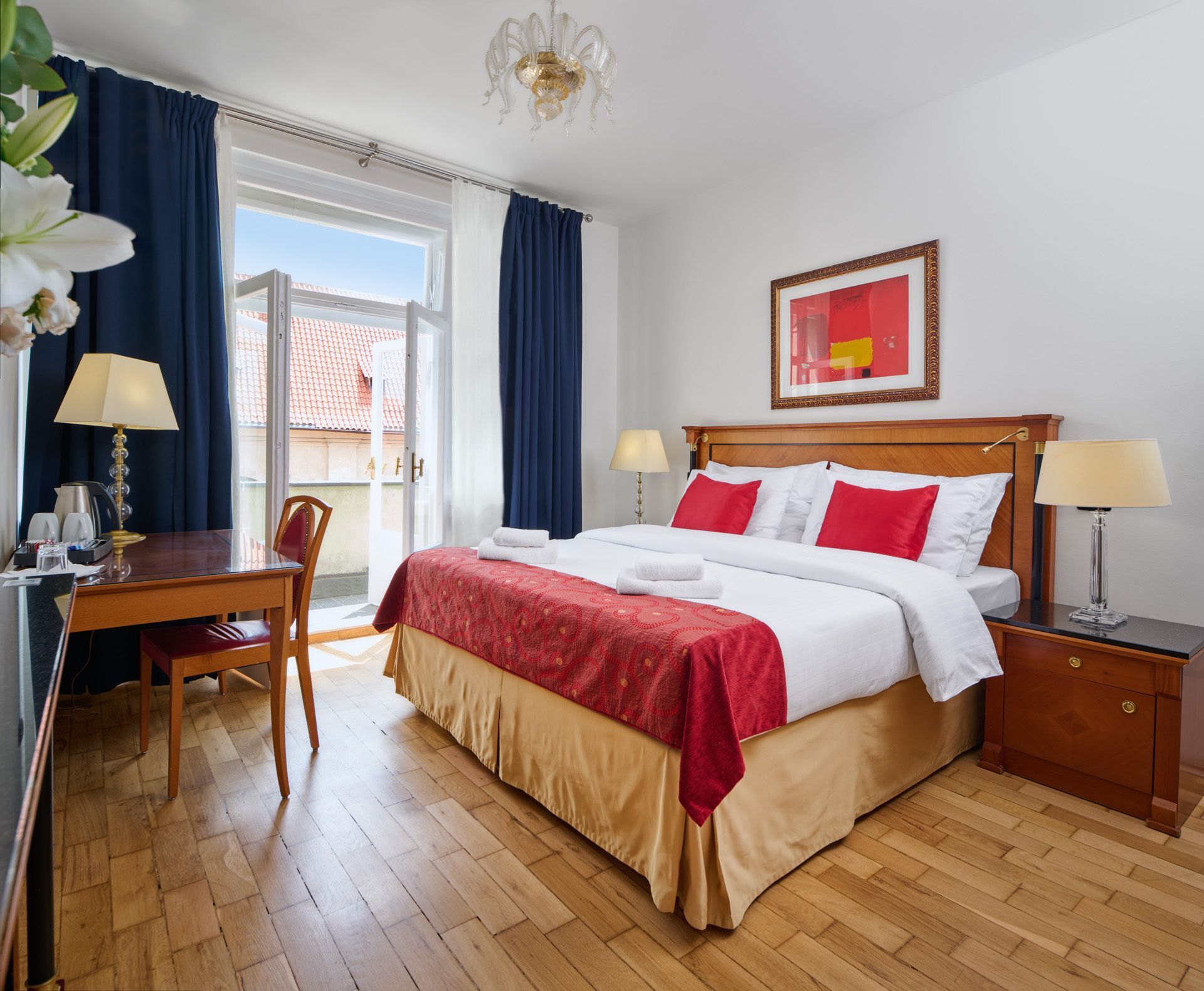 Hotel room corner with TV, desk, chair, lamp, and armchair on red carpet.