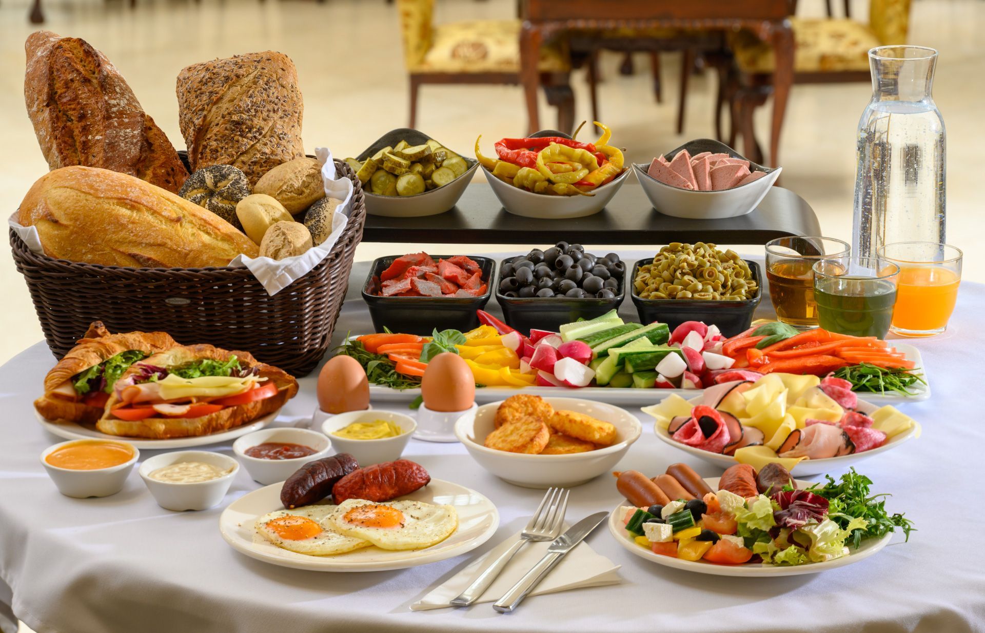 People eating breakfast: eggs, bacon, beans, croissant, coffee, orange juice, on a table.