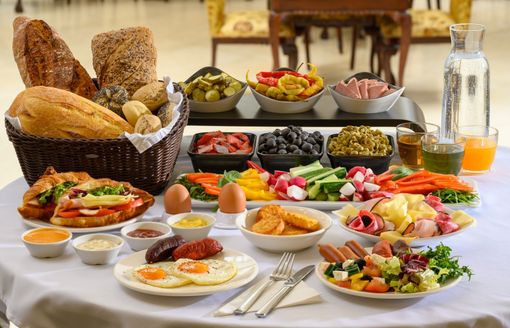 People eating breakfast: eggs, bacon, beans, croissant, coffee, orange juice, on a table.