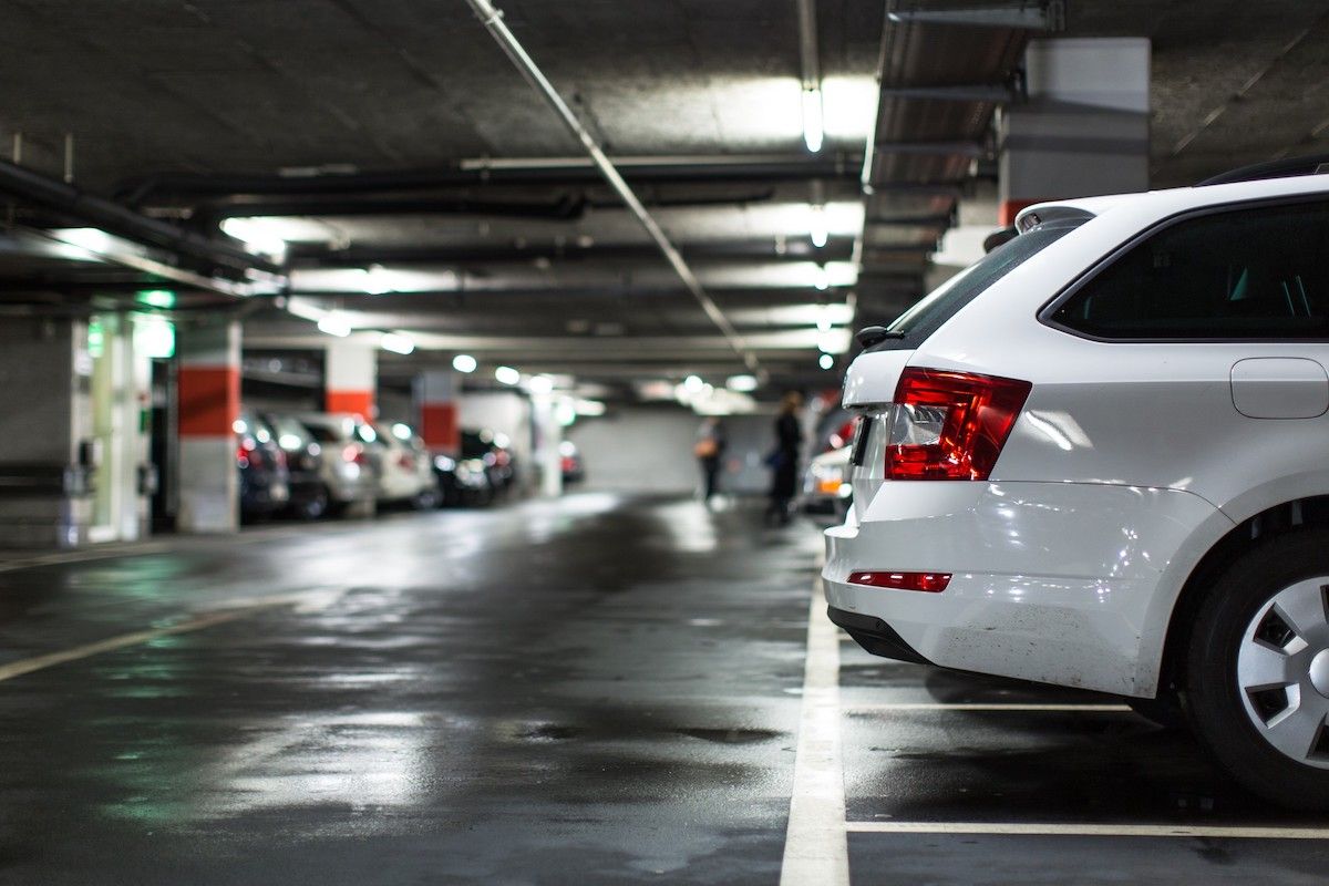 White car parked in an underground parking garage. Dark, wet pavement, other cars, and people are in the background.