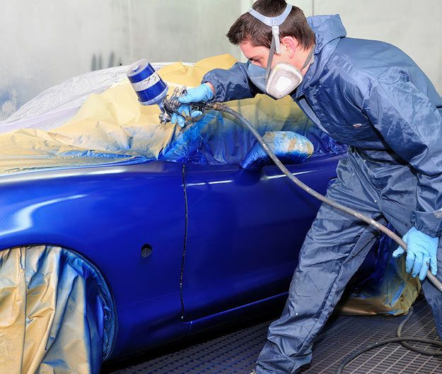 Apprentice mechanic spray painting car carefully ocean blue