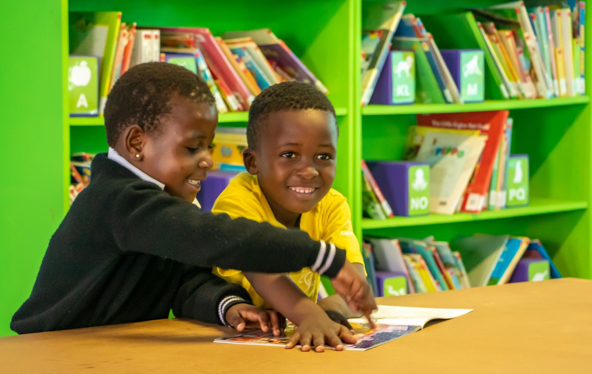 Two young boys are reading a book together in a library.