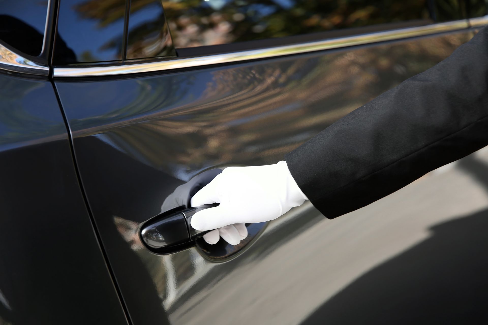 A person wearing white gloves is opening the door of a black car.