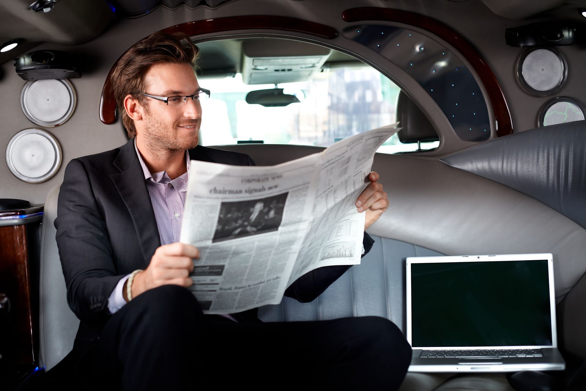 A man in a suit is reading a newspaper in a car