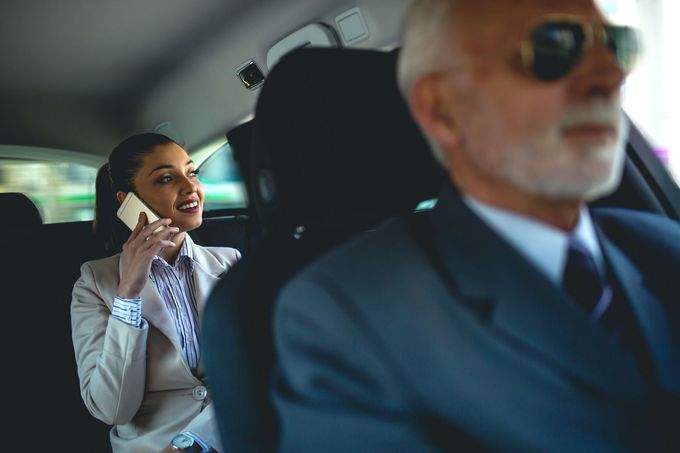 A woman is sitting in the back seat of a car talking on a cell phone.