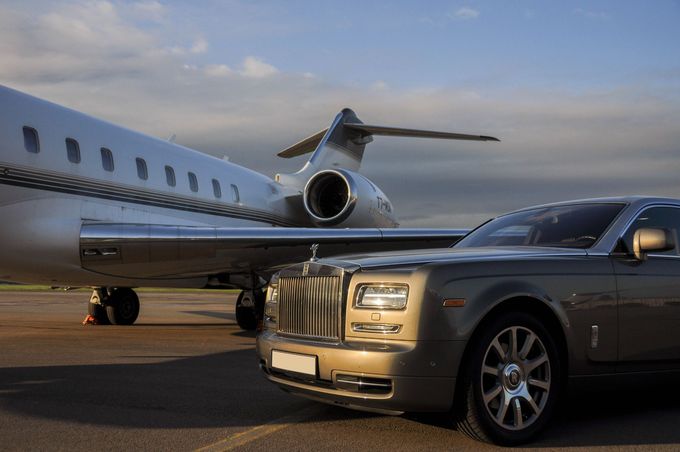 A car is parked next to a private jet on a runway.