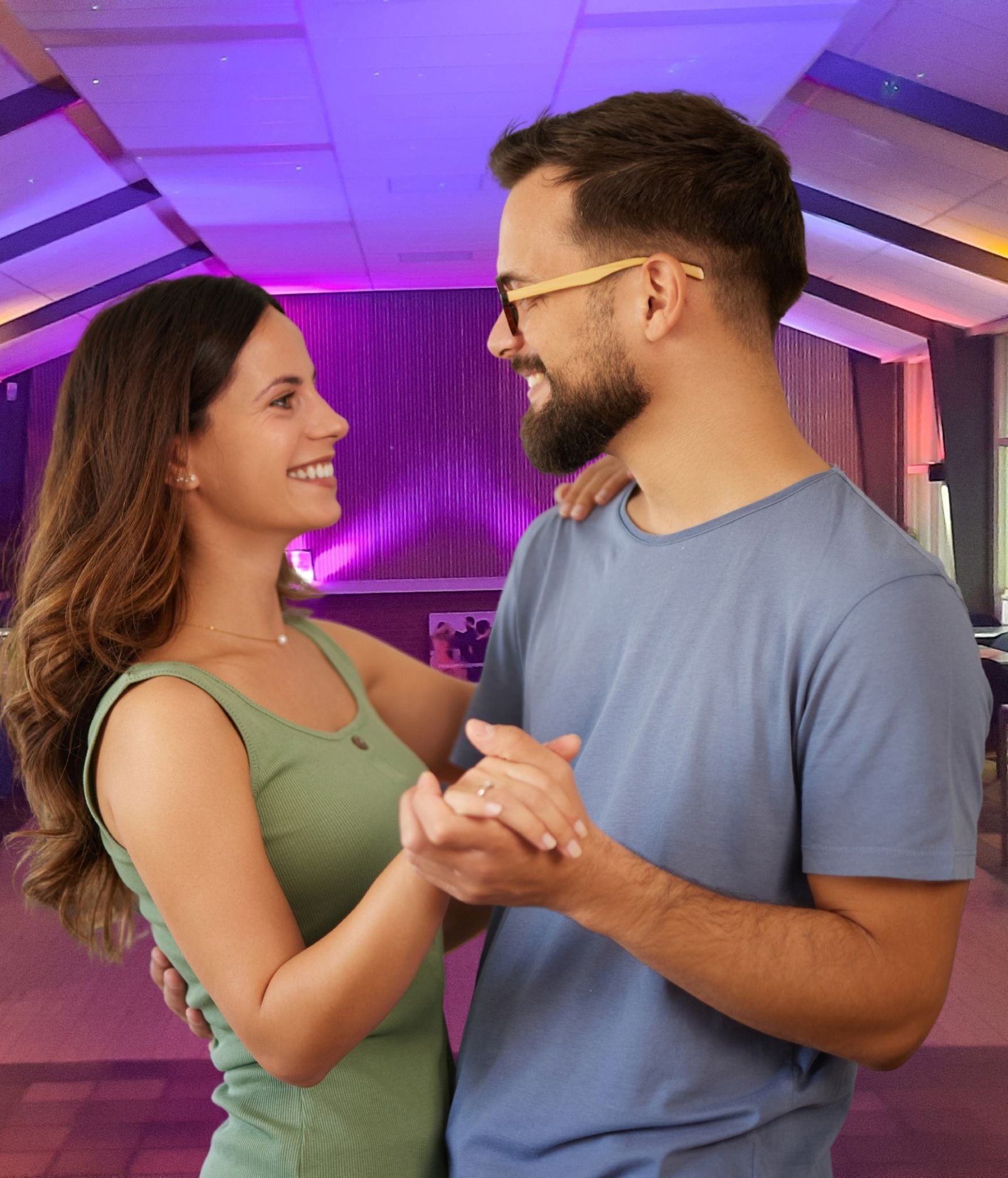 Een man en een vrouw dansen heel dicht op elkaar, lachend, in een balzaal met andere paren.