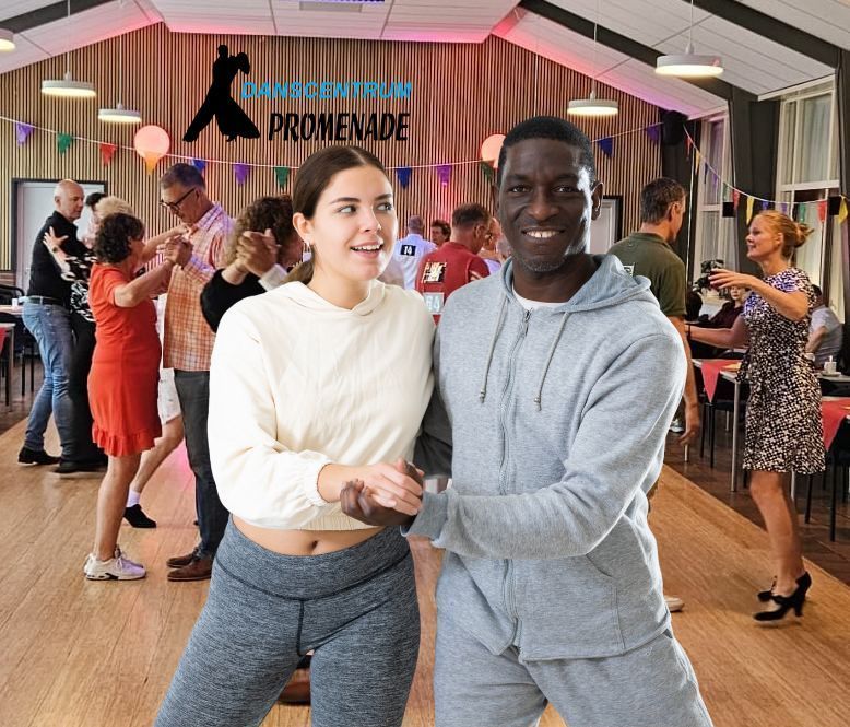 Een lachend stel danst in een dansstudio met anderen. Lichte houten vloer, feestversiering.