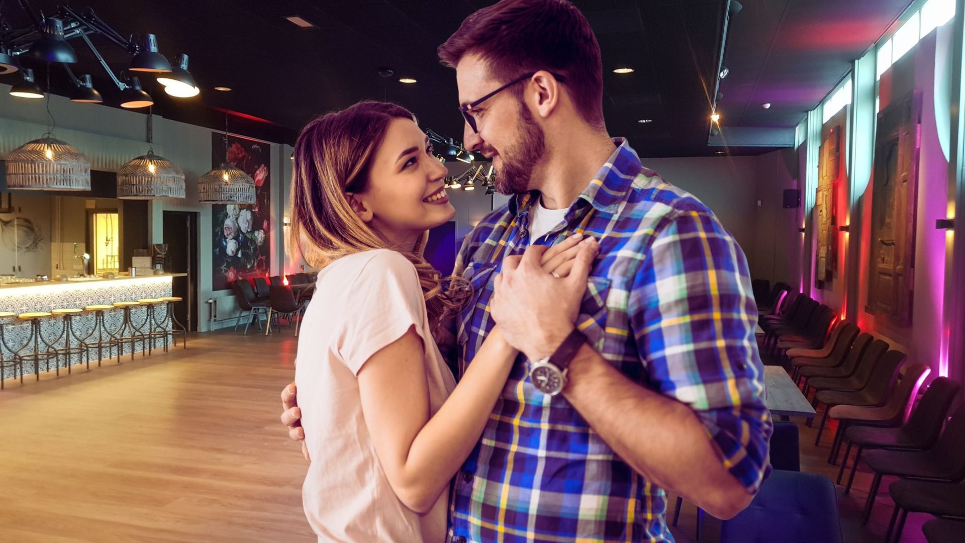 Man en vrouw omhelzen elkaar in een dansstudio en kijken elkaar met liefdevolle blikken aan.