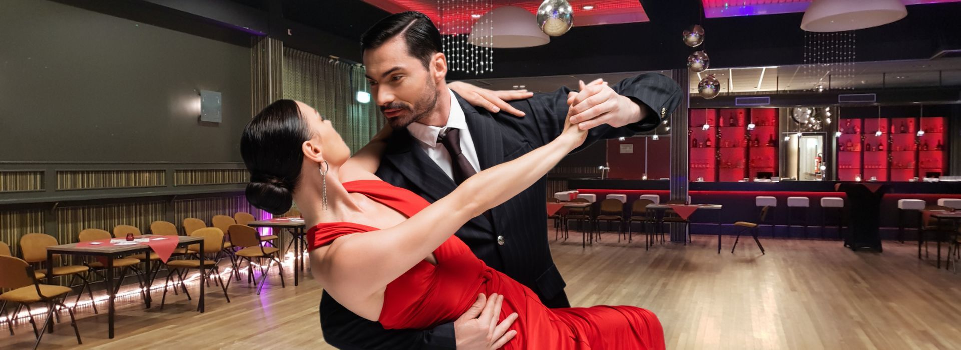 Een paar dansend in een balzaal, de vrouw in een rode jurk, de man in een pak. Ze hebben een serieuze blik.