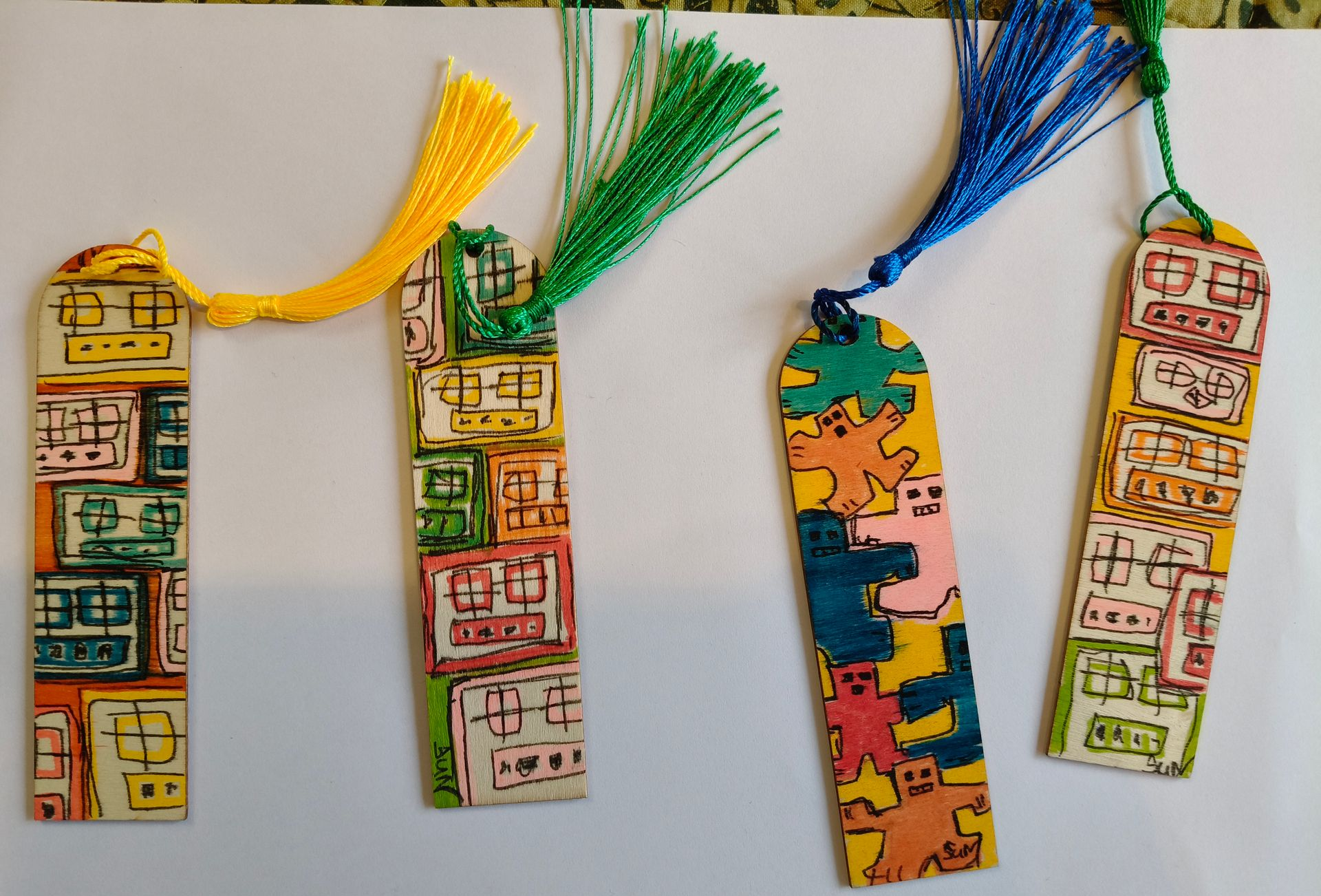 Vier handgemaakte bladwijzers met kleurrijke, handgetekende patronen en kwastjes in geel, groen, blauw en geel.