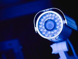 Security camera, blue-tinted, focused on lens, mounted on bracket.