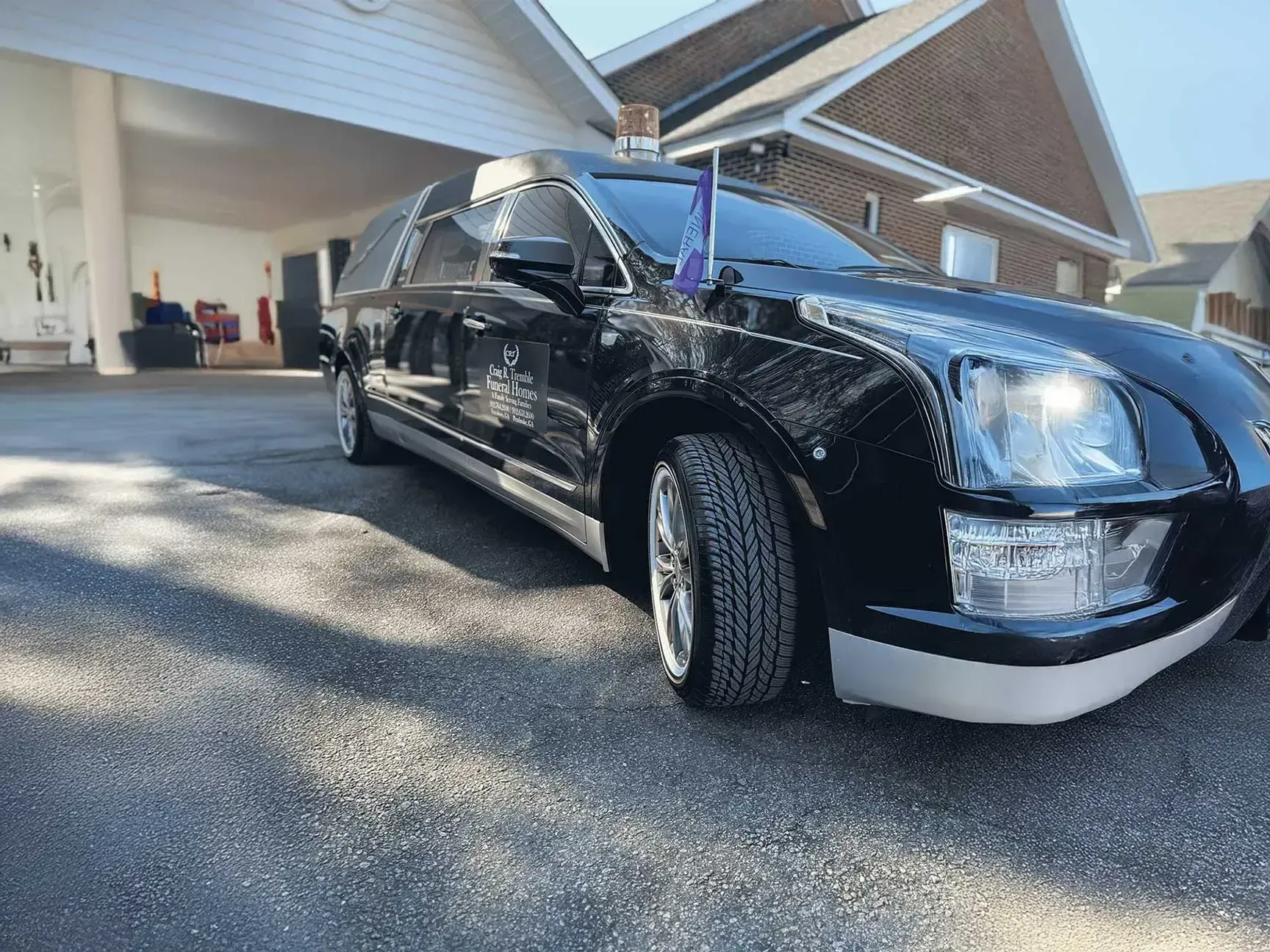 Black hearse parked on asphalt driveway, in front of a white building.