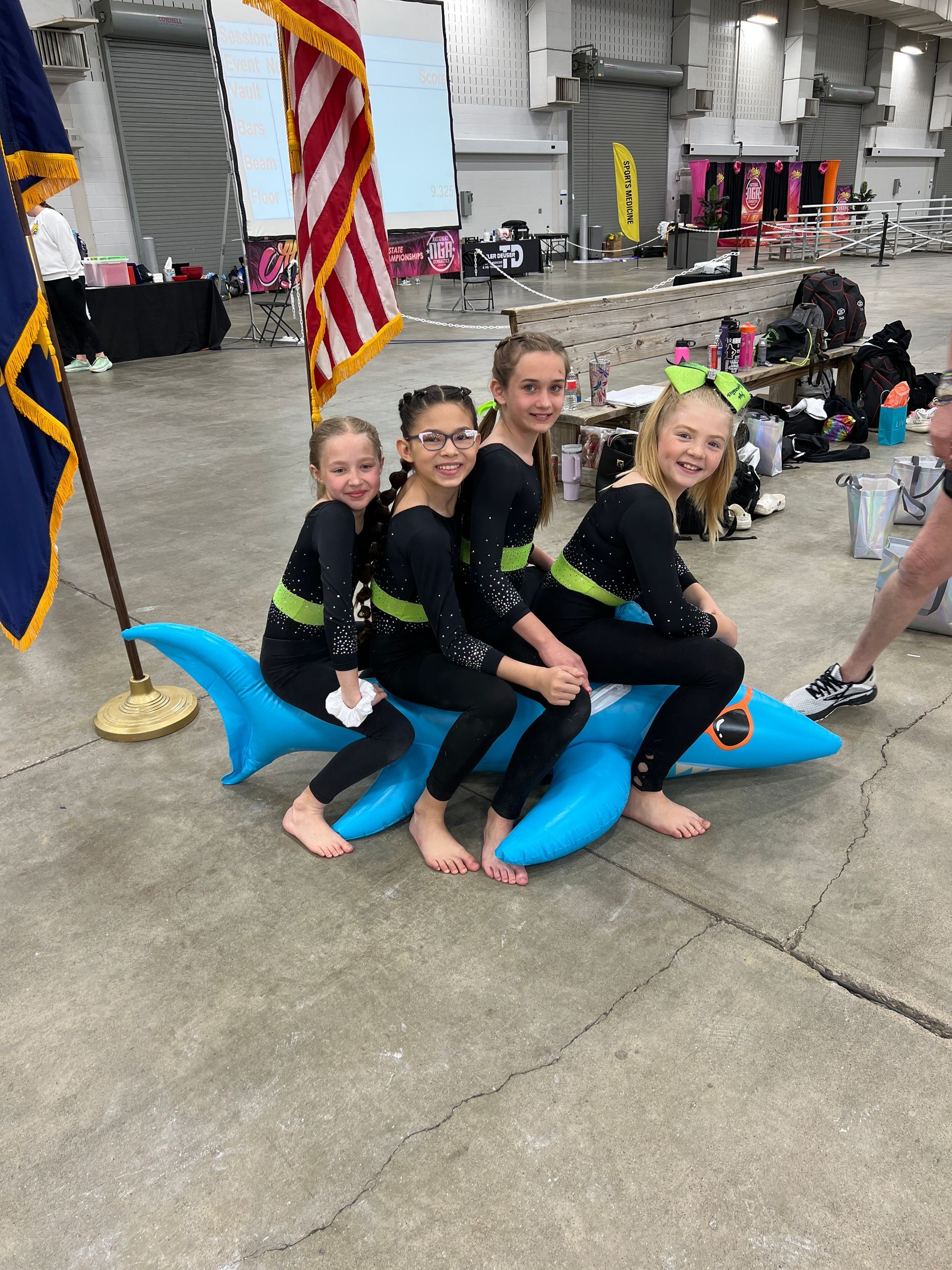 Three young girls are sitting on a blue inflatable dolphin.