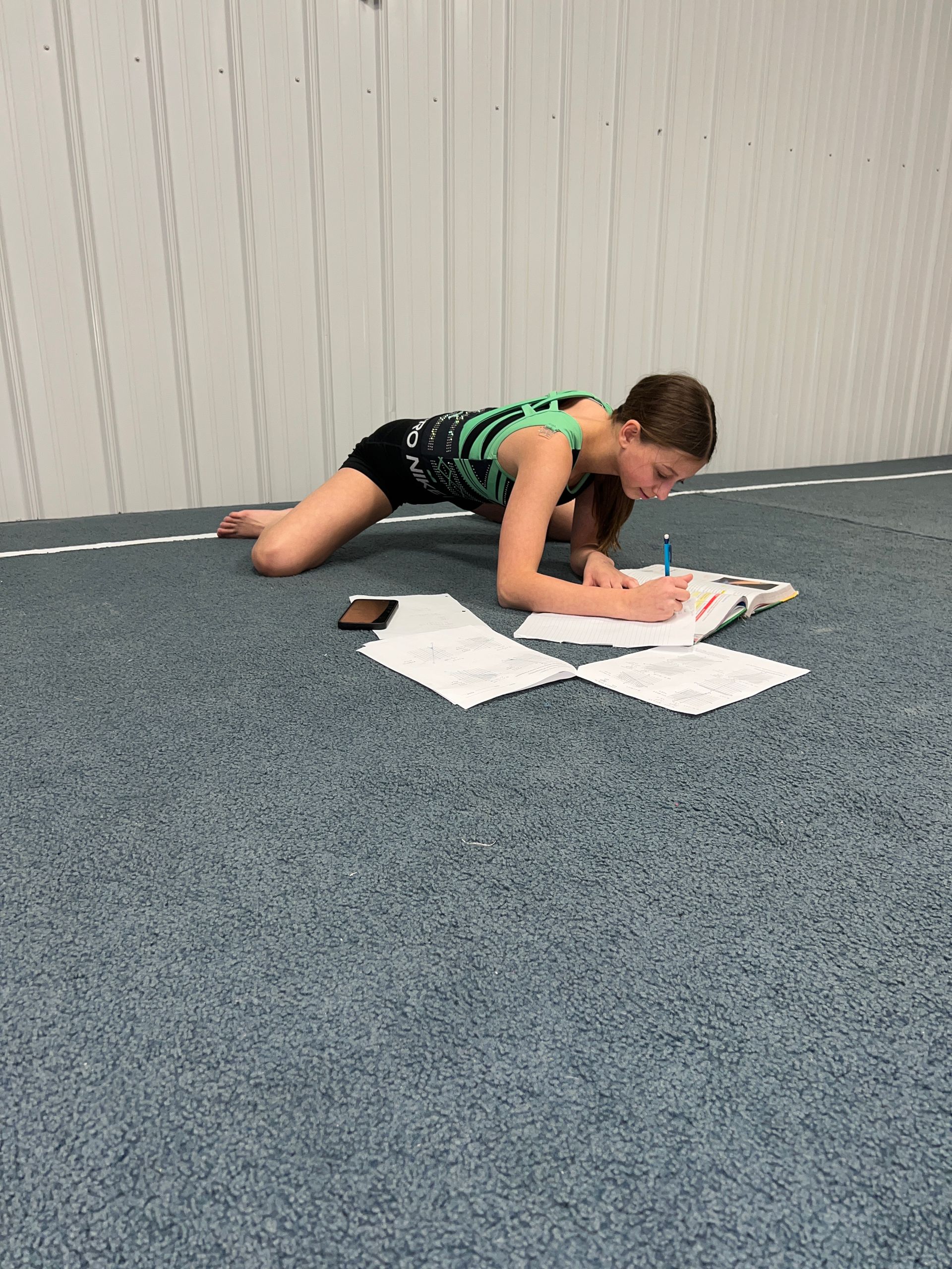 A young girl is laying on the floor writing in a notebook.