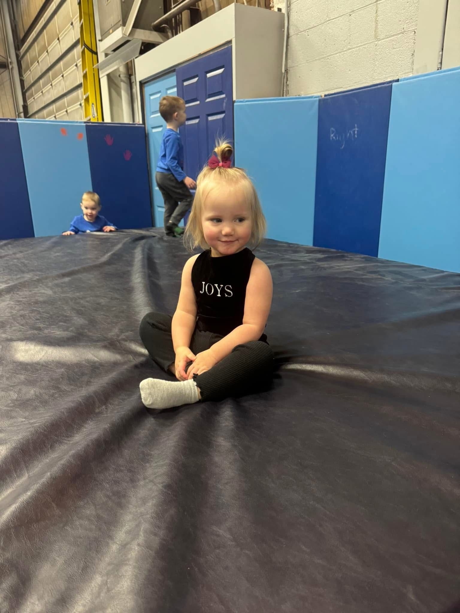 A little girl is sitting on a trampoline in a gym.