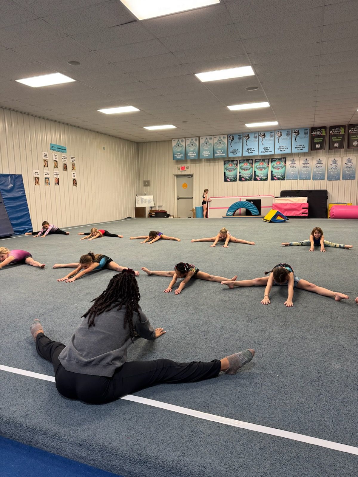 A group of girls are doing splits on the floor in a gym.