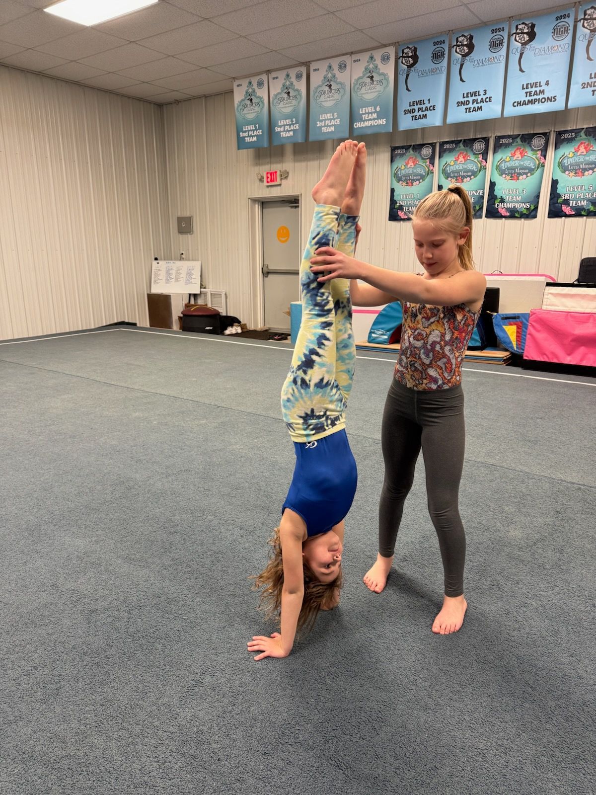 Two young girls are doing a handstand in a gym.