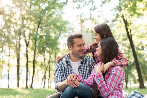 Familia de tres en un parque, sonriendo y abrazándose.
