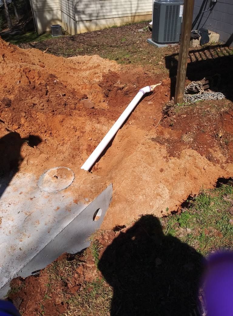 Excavated dirt beside a house with a white PVC pipe and exposed utility equipment.