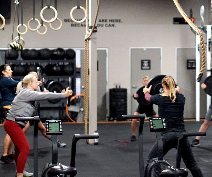 People exercising in a gym class, using rowing machines and swinging gymnastic rings.