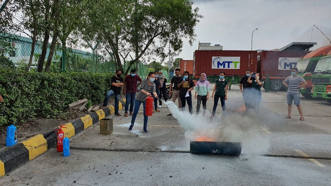 Group of people putting out a fire with extinguishers; in front of a truck, and barriers.