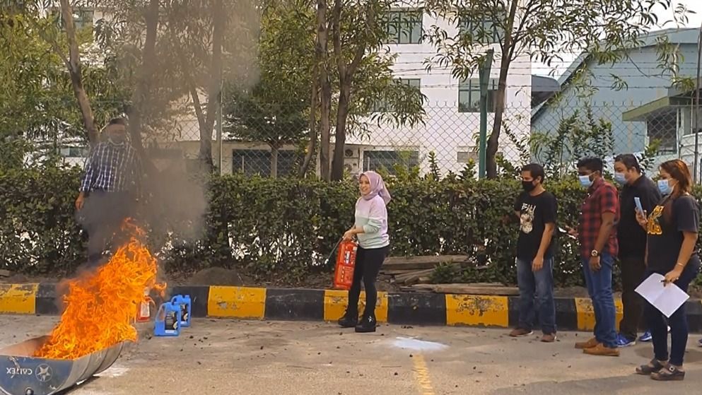 Fire safety demonstration: Person uses a fire extinguisher on a controlled fire, with onlookers wearing masks.