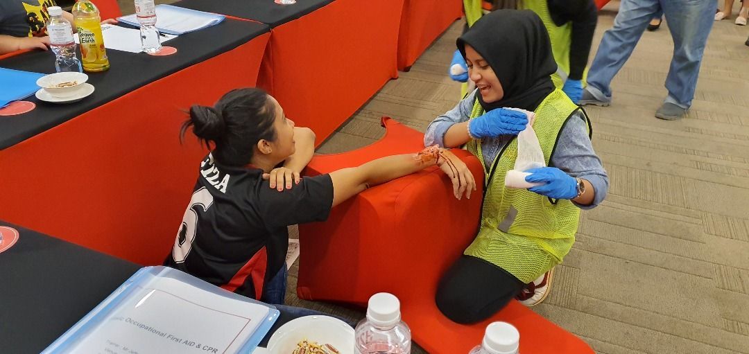 A person in a hijab and safety vest tends to another person's arm on a red surface.