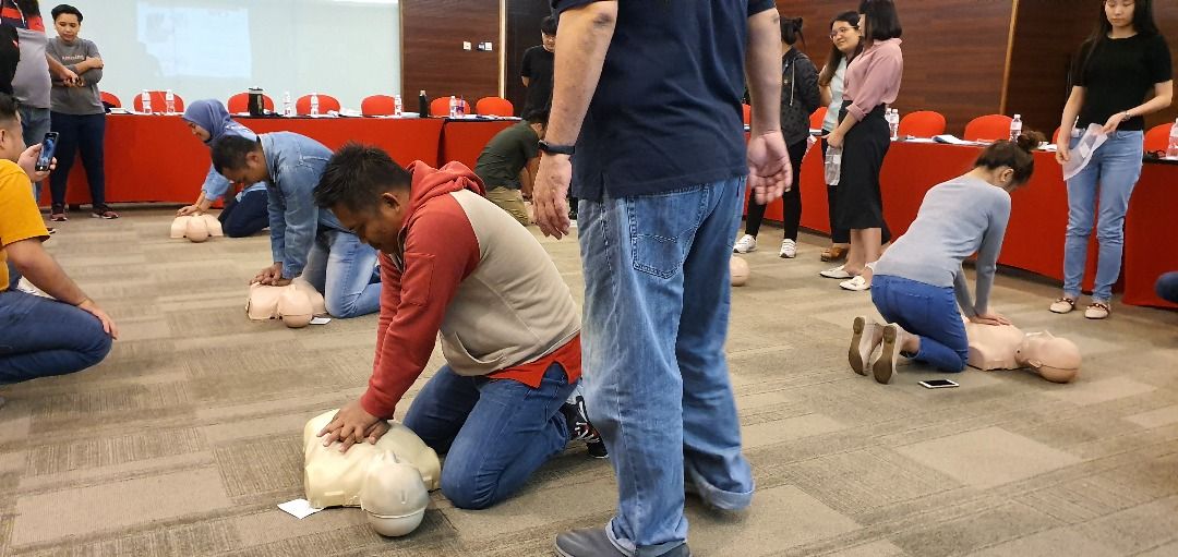 People practicing CPR on mannequins during a training session in a conference room.