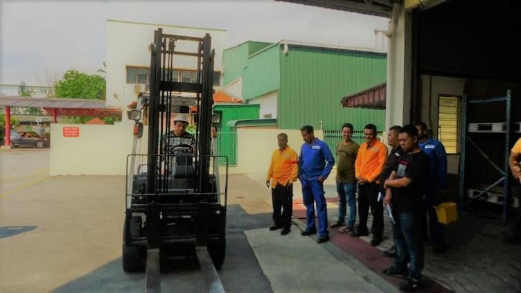 Forklift operator in training with an audience in a loading dock setting.