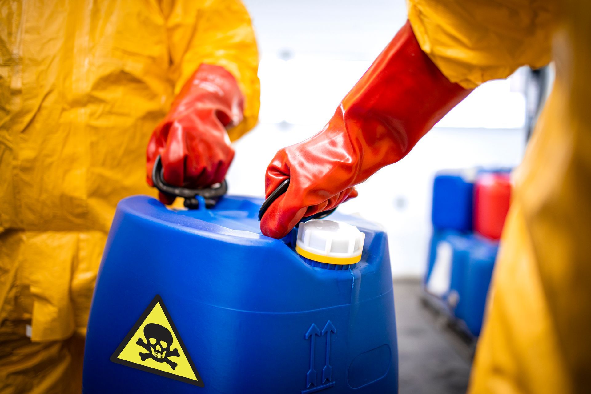 Two people in protective suits open a blue container with a skull and crossbones warning label.