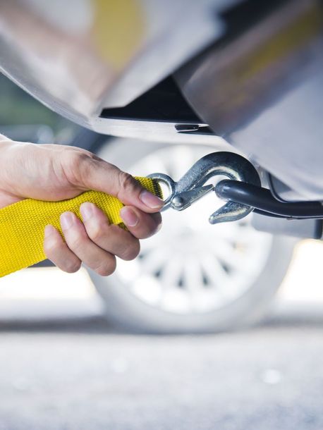 A person is towing a car with a yellow tow strap.