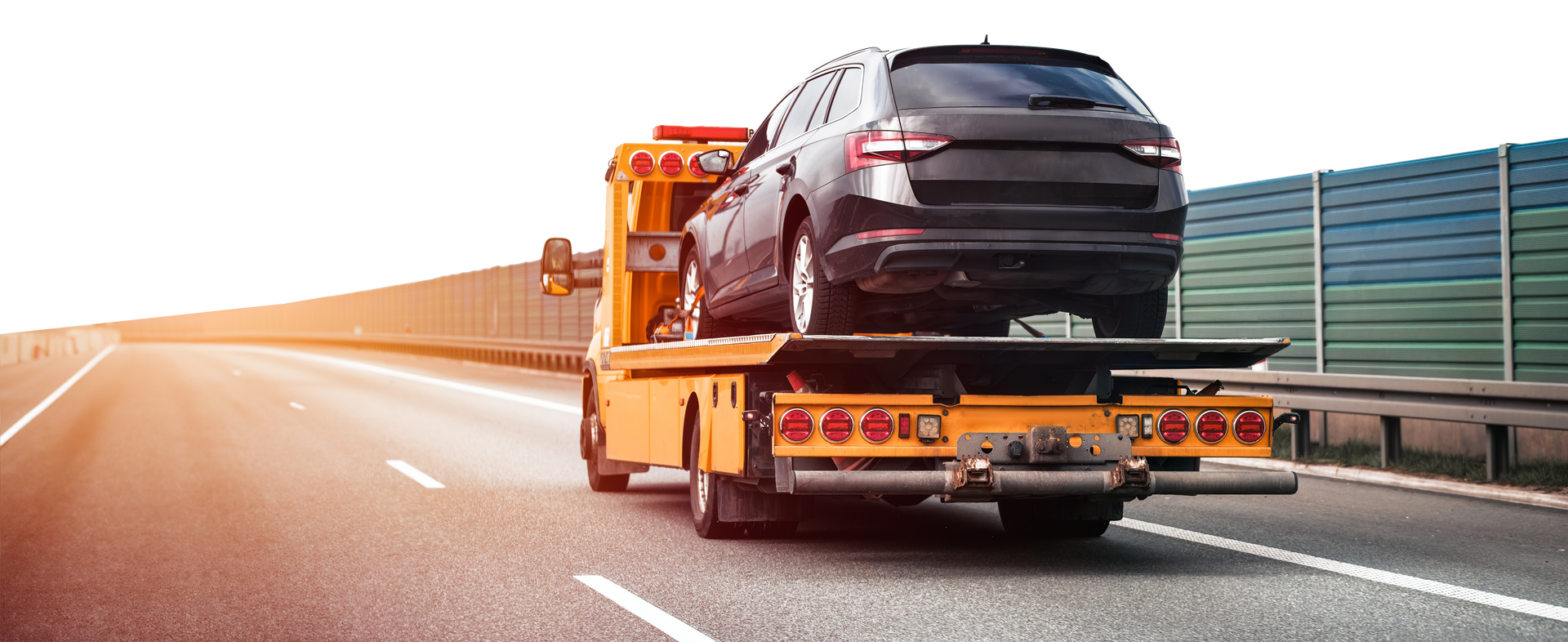 A car is being towed down a highway by a tow truck.