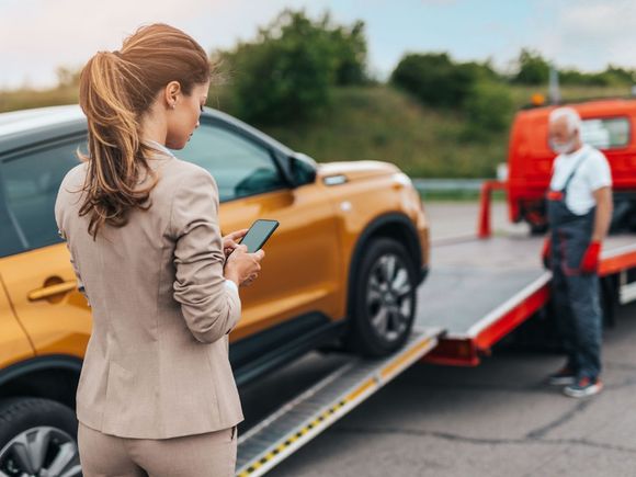 A woman is standing next to a tow truck with a car on it.