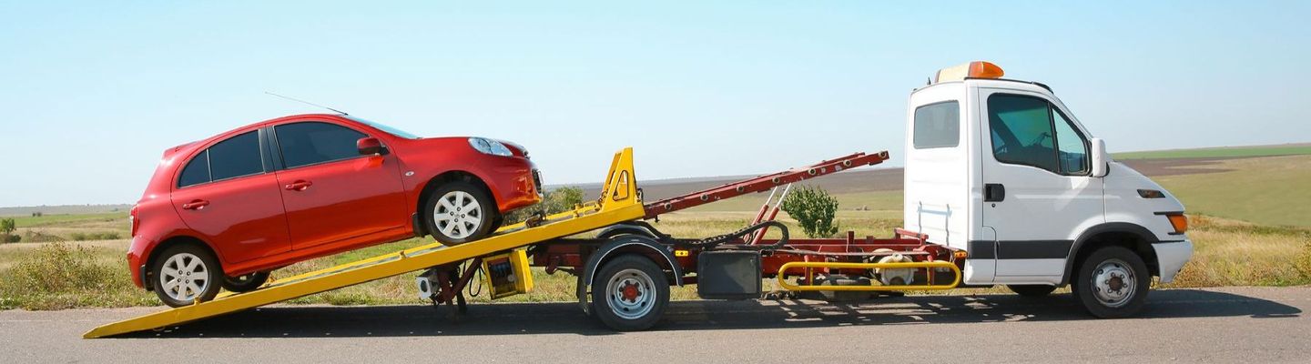 A red car is being towed by a tow truck on the side of the road.