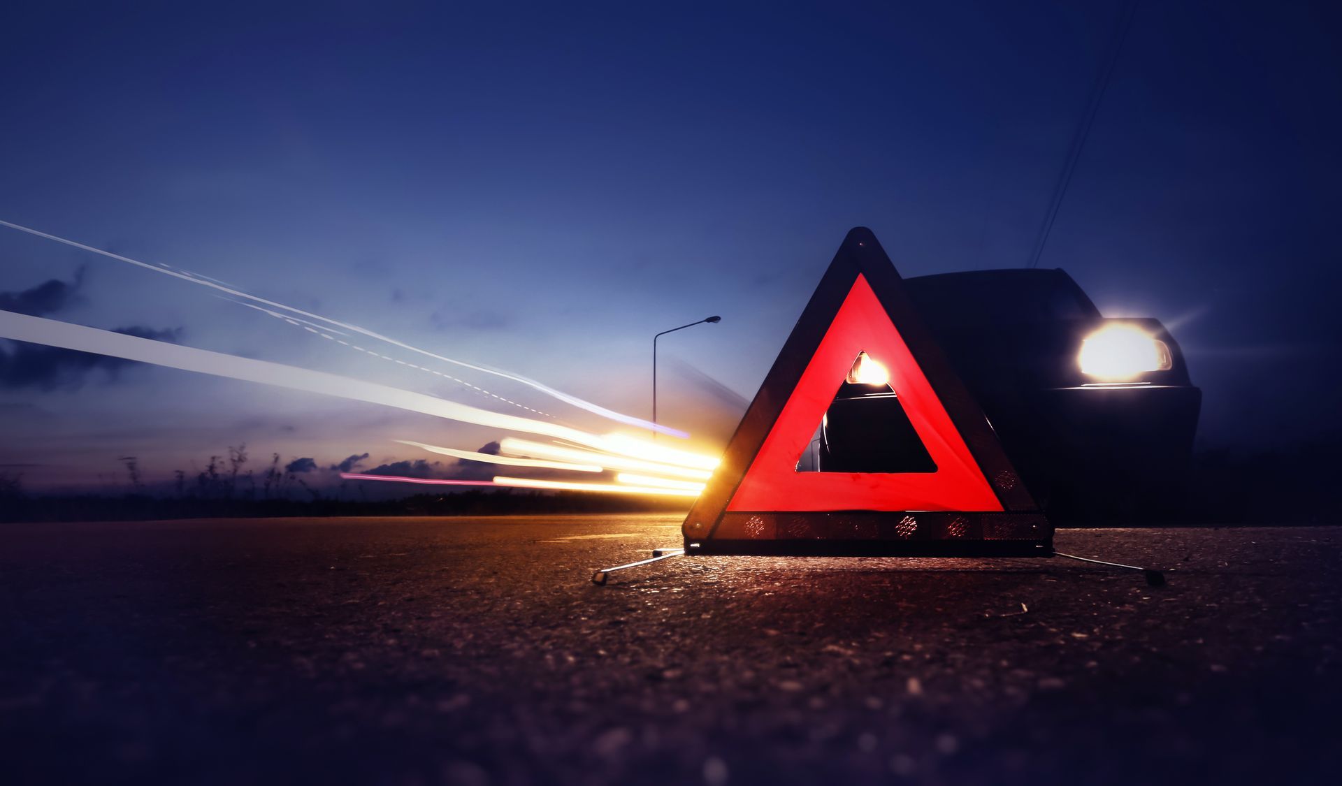 A red triangle with a car in the background is lit up at night