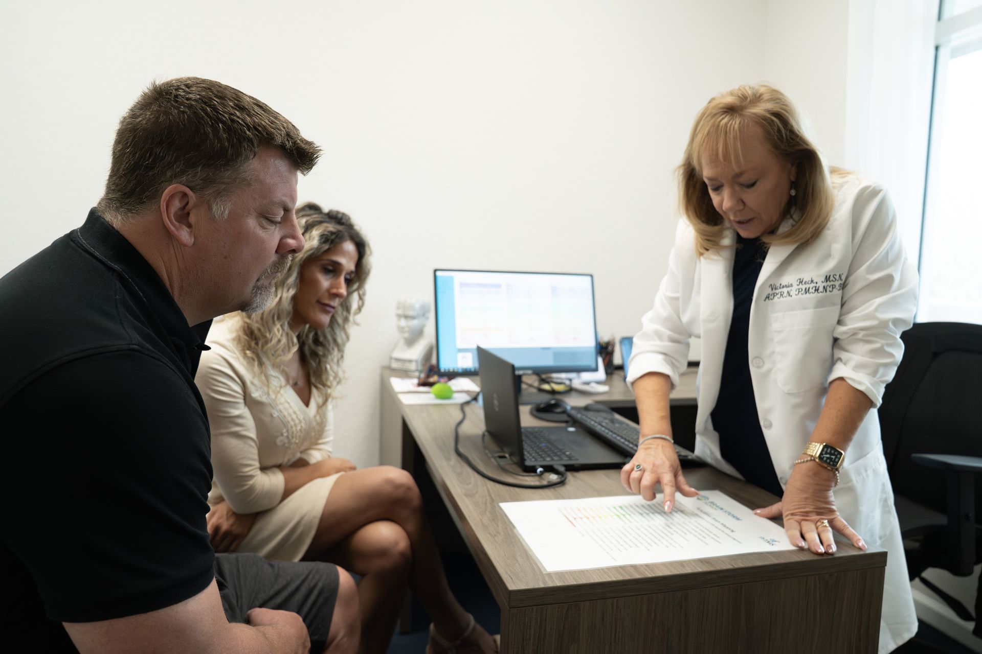 A doctor in a white coat reviews papers with a couple in an office.