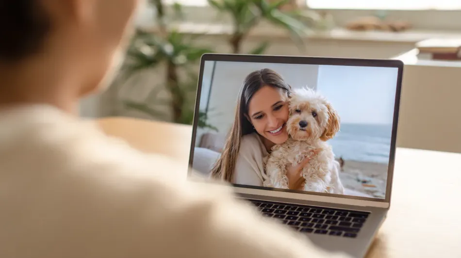 Person on a video call with a woman holding a dog, smiling, in a room with ocean views.