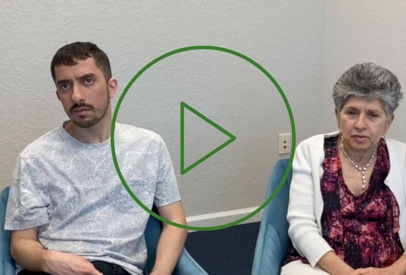 Two people seated, a man in a patterned shirt and a woman in a cardigan, in an office, ready to start a video.