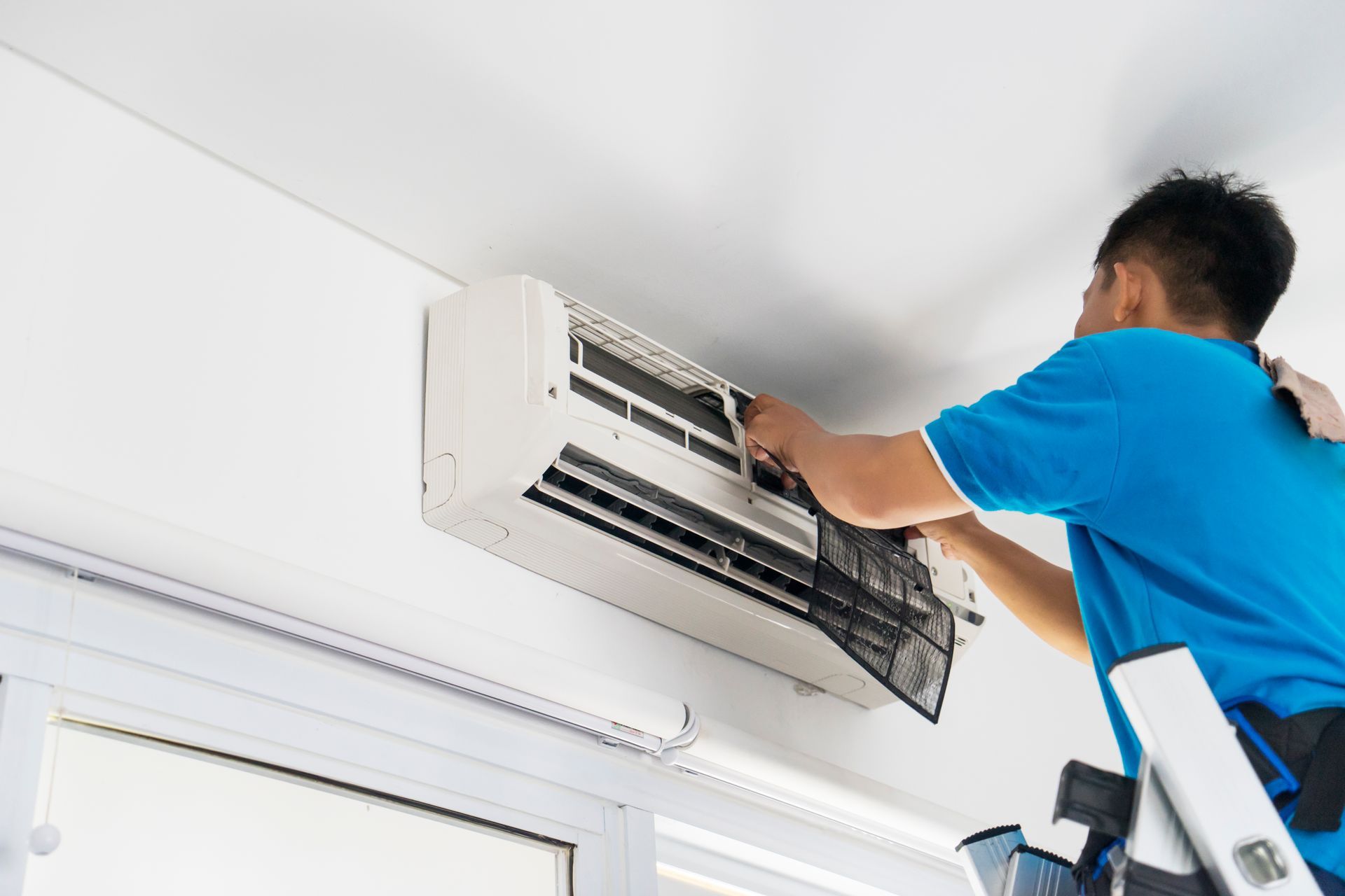 HVAC technician kneels to service an outdoor air conditioning unit. Using tools, he tests wiring outdoors in a yard.