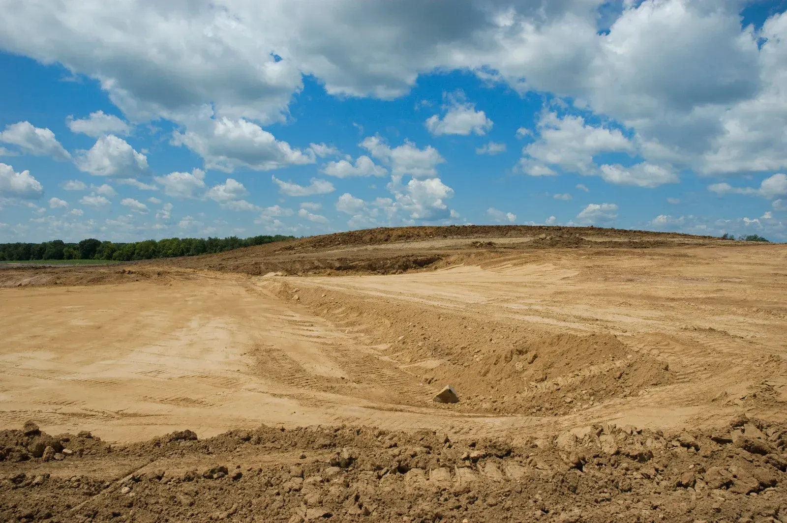 Construction site with heavy machinery, a yellow excavator, and a cement mixer truck under a clear blue sky.