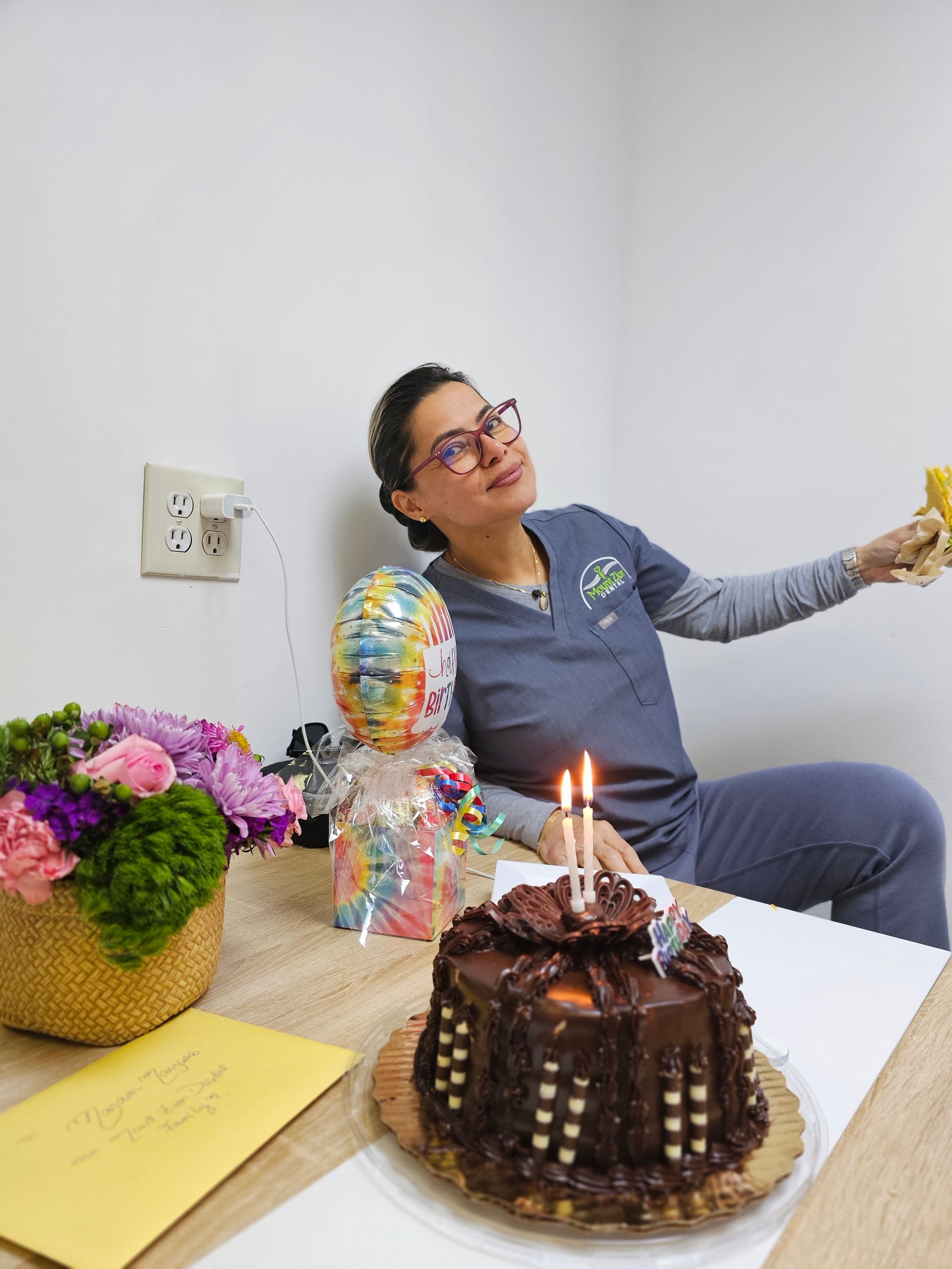 A woman is sitting at a table with a cake and balloons